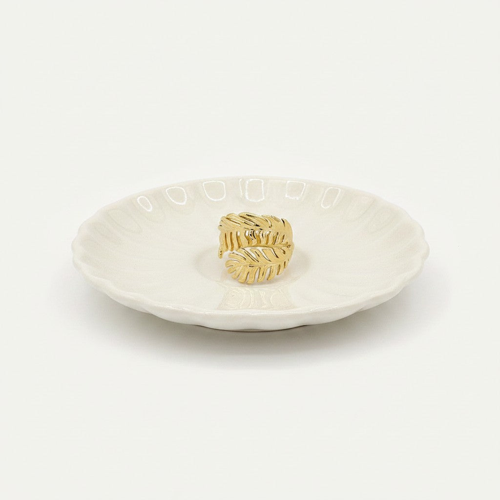 Bague ajustable Ipsē en acier inoxydable doré avec motif de deux feuilles exotiques posée sur une coupelle blanche
